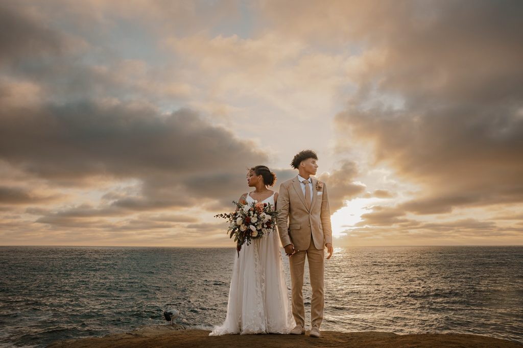 San Diego bride and groom pose for portrait on cliff at sunset