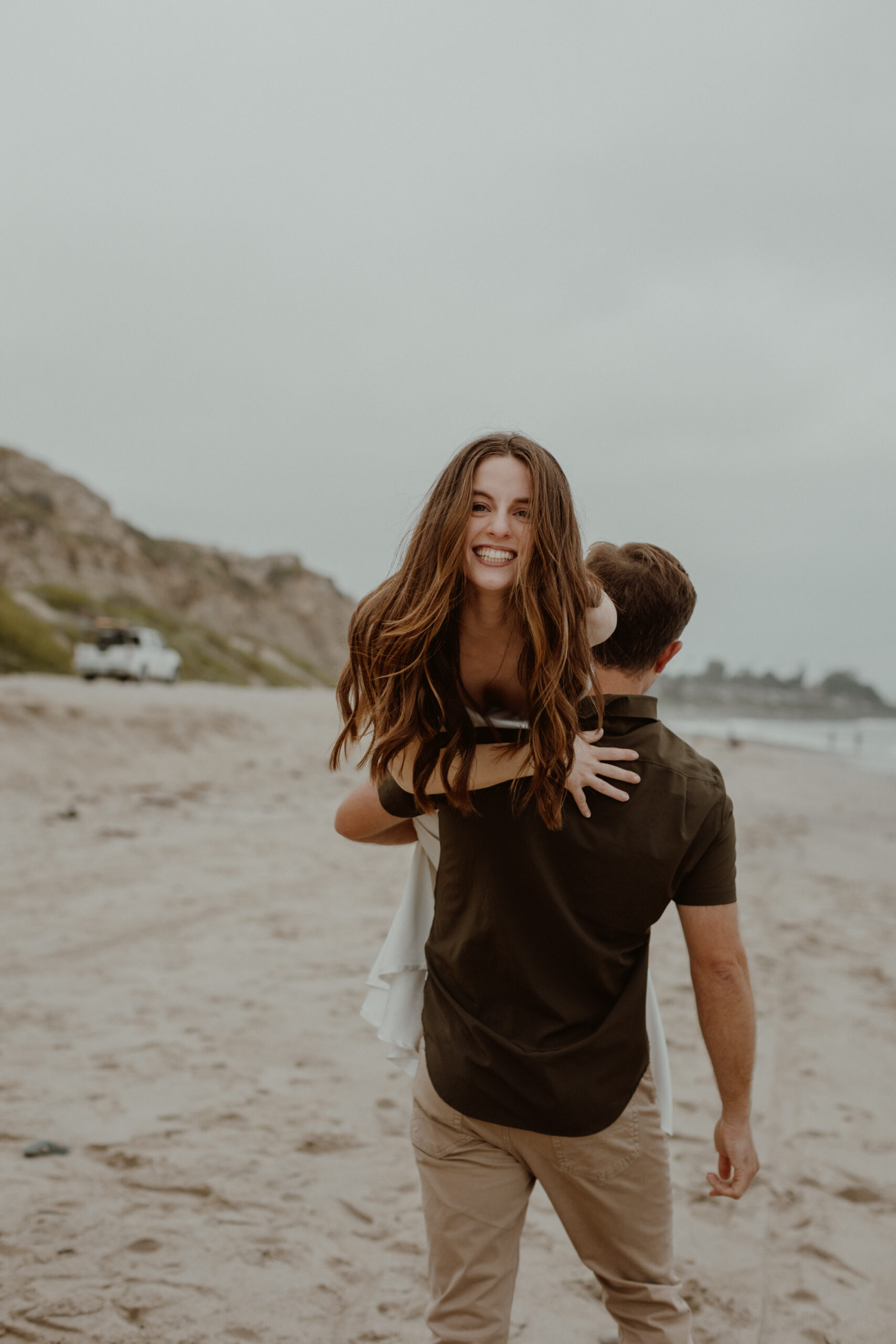 couple plays while taking engagement photo on the beach in San Clemente